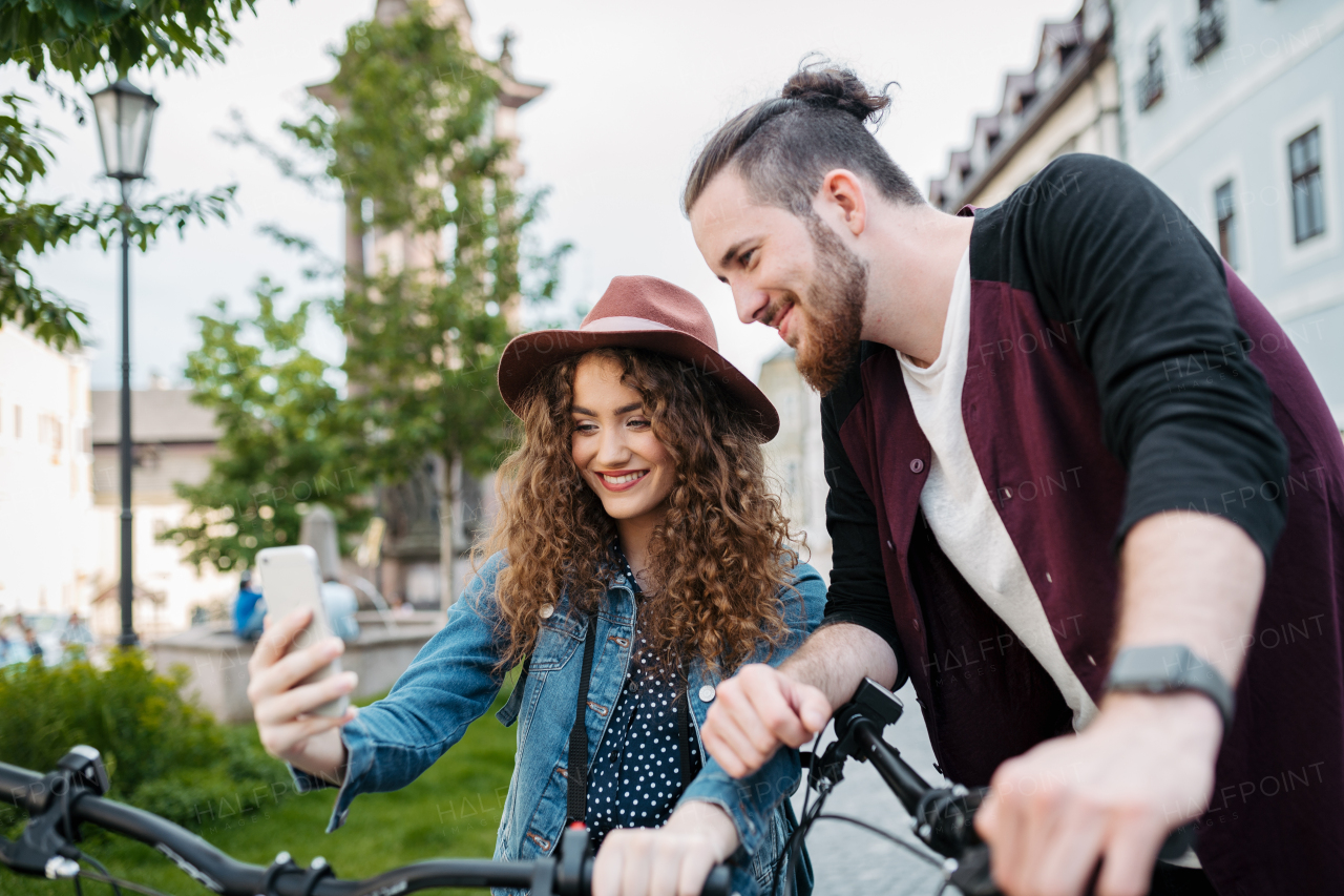 Travellers couple taking selfie, standing by electric scooters in city, sightseeing. Young tourist using bikes during their summer trip, vacation.