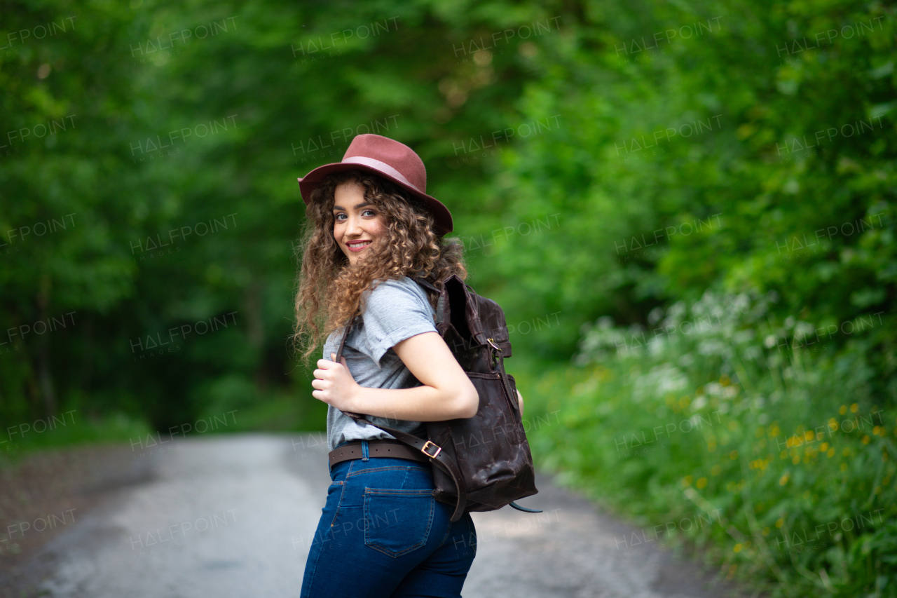 Beautiful young tourist woman traveller with backpack walking in nature. Active female hiker on trail in woods. Solo summer vacation.