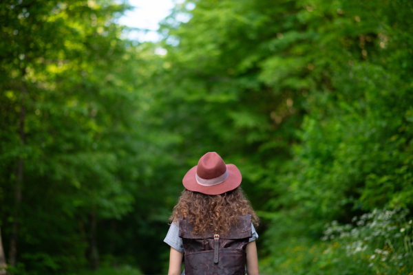 Rear view of young tourist woman traveller with backpack walking in nature. Active female hiker on trail in woods. Solo summer vacation.