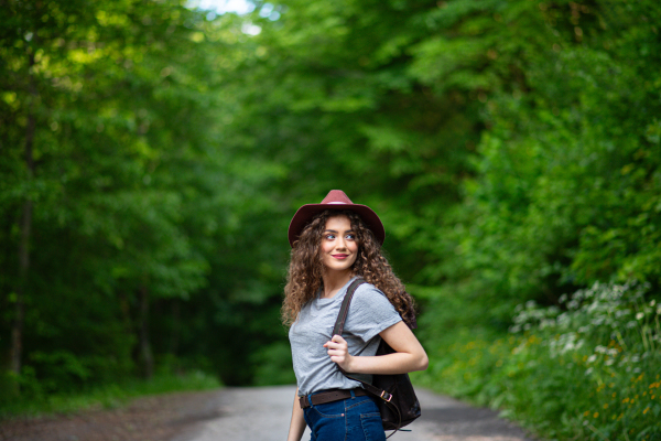 Beautiful young tourist woman traveller with backpack walking in nature. Active female hiker on trail in woods. Solo summer vacation.