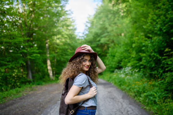 Beautiful young tourist woman traveller with backpack walking in nature. Active female hiker on trail in woods. Solo summer vacation.