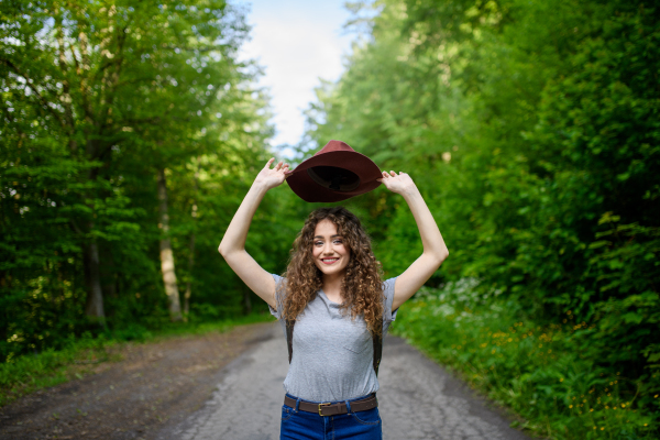 Beautiful young tourist woman traveller with backpack walking in nature. Active female hiker on trail in woods. Solo summer vacation.