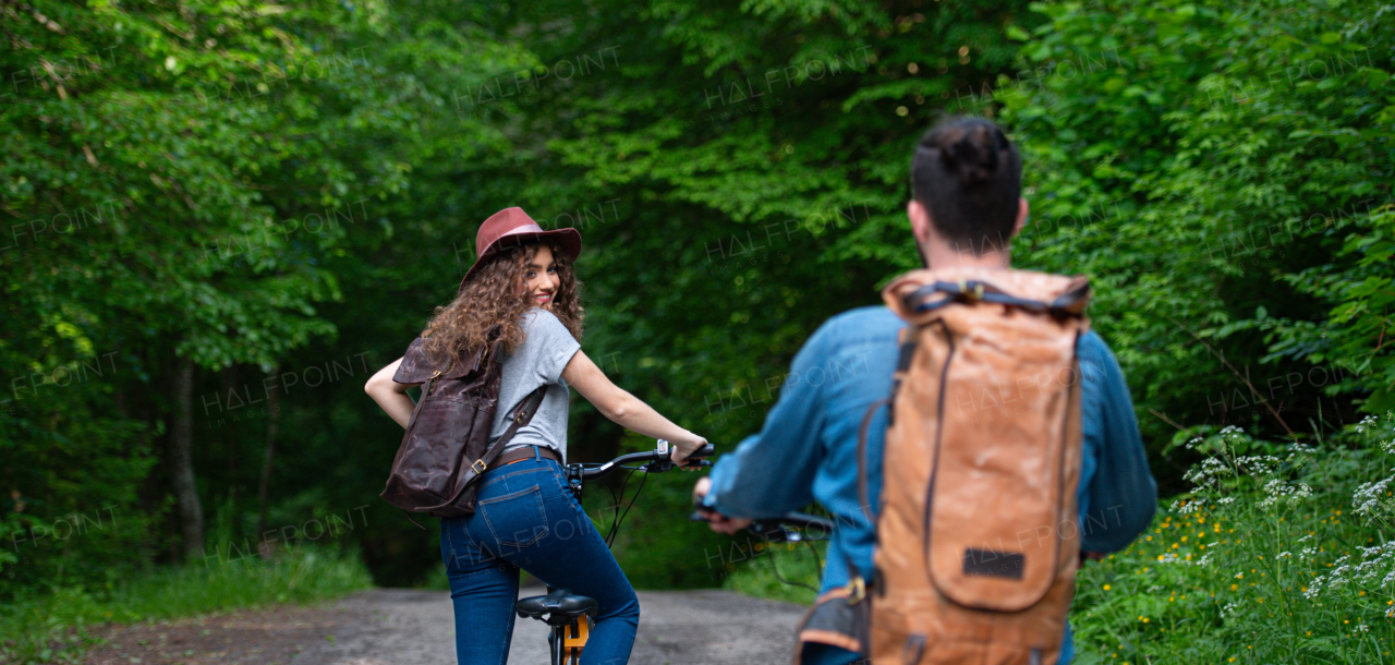 Travellers couple going on e-bike ride in nature. Tourist riding electric bicycles on easy trail road in the middle of forest. Young tourist spending romantic summer vacation oudoors.