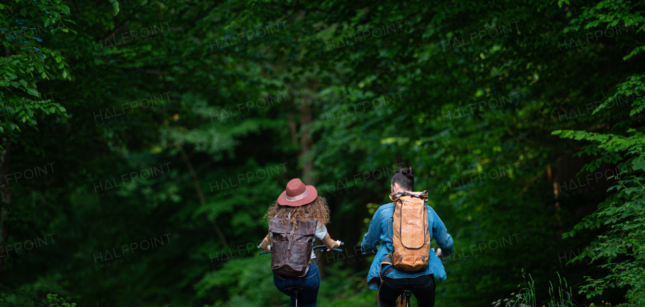 Travellers couple going on e-bike ride in nature. Tourist riding electric bicycles on easy trail road in the middle of forest. Young tourist spending romantic summer vacation oudoors.