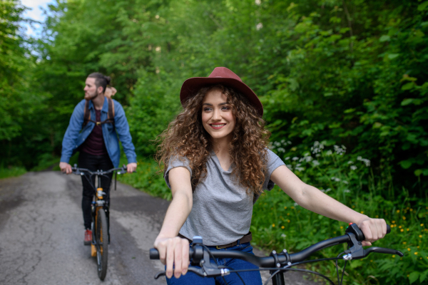 Travellers couple going on e-bike ride in nature. Tourist riding electric bicycles on easy trail road in the middle of forest. Young tourist spending romantic summer vacation oudoors.