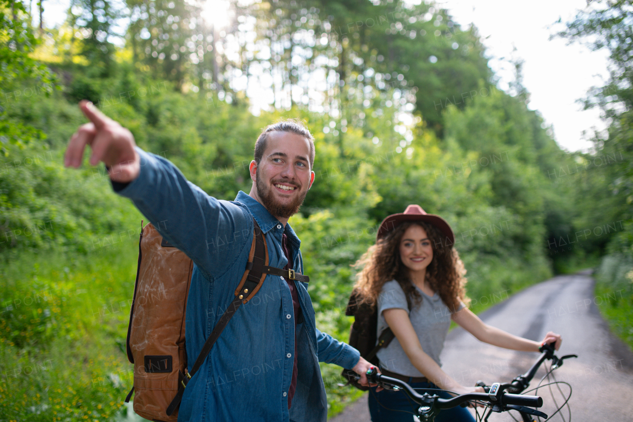 Travellers couple going on e-bike ride in nature. Tourist riding electric bicycles on easy trail road in the middle of forest. Young tourist spending romantic summer vacation oudoors.