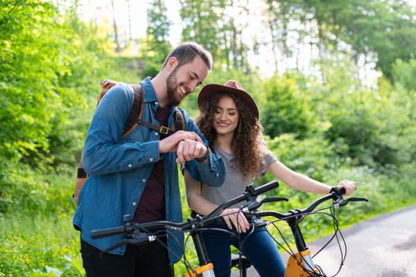 Travellers couple going on e-bike ride in nature. Tourist riding electric bicycles on easy trail road in the middle of forest. Young tourist spending romantic summer vacation oudoors.