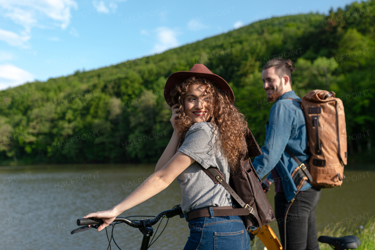 Travellers couple going on e-bike ride in nature. Tourist riding electric bicycles on easy trail road by lake. Young tourist spending romantic summer vacation oudoors.