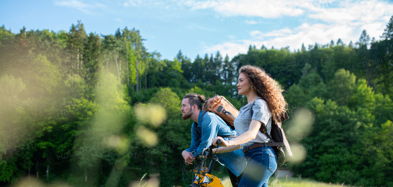 Travellers couple going on e-bike ride in nature. Tourist riding electric bicycles on easy trail road in the middle of forest. Young tourist spending romantic summer vacation oudoors.