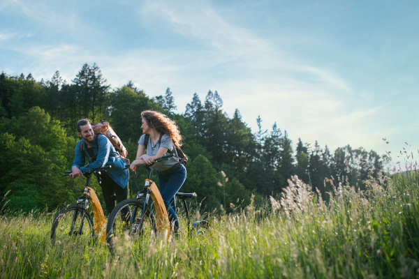 Travellers couple going on e-bike ride in nature. Tourist riding electric bicycles on easy trail road in the middle of forest. Young tourist spending romantic summer vacation oudoors.