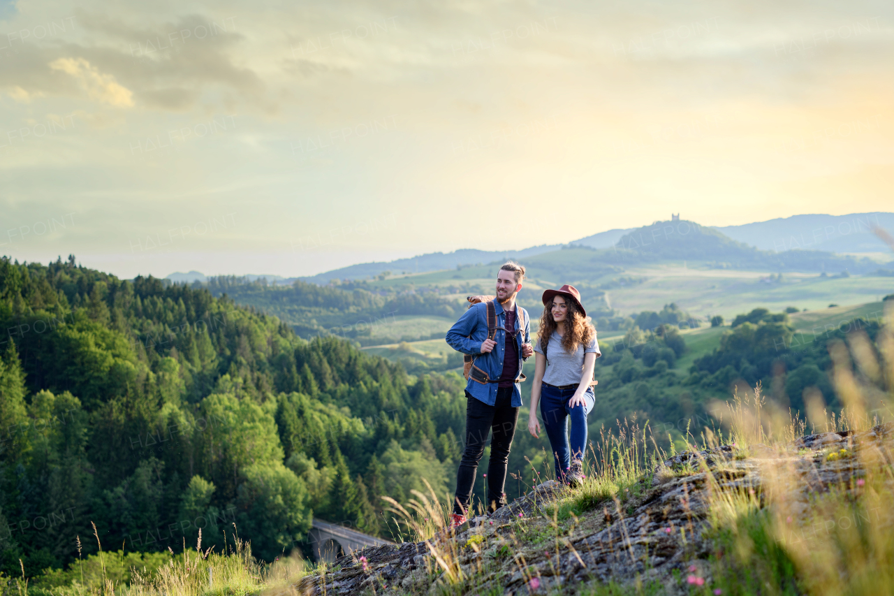 Travellers couple hiking on easy trail in nature with backpacks. Young tourist resting, enjoying breathtaking view. Romantic summer vacation oudoors. Rear view.