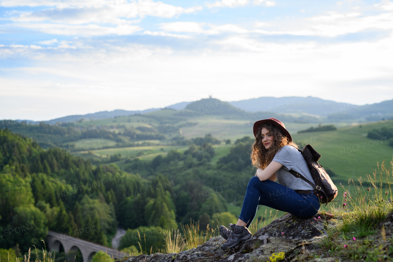 Beautiful tourist woman traveller with backpack in nature, sitting and resting. Active hiker on trail in mountains enjoying breathtaking view. Solo summer vacation.