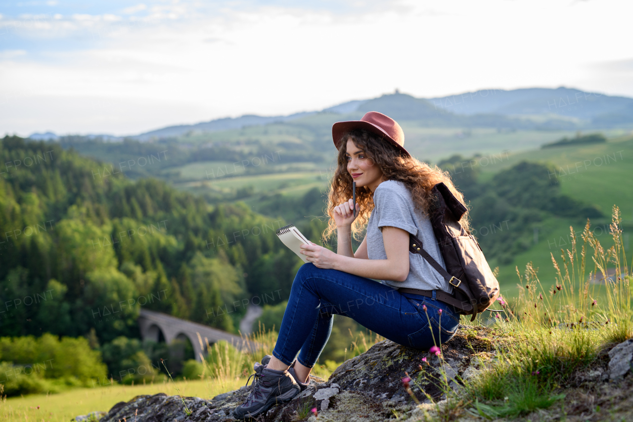 Beautiful tourist woman traveller with backpack in nature, sitting and resting. Active hiker on trail in mountains enjoying breathtaking view. Solo summer vacation.