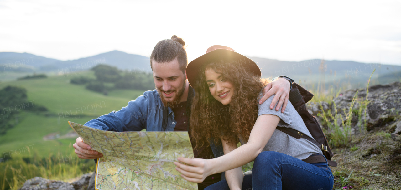 Travellers couple hiking on easy trail in nature with backpacks. Young tourist resting, looking for route in map and drinking water. Banner with copy space.