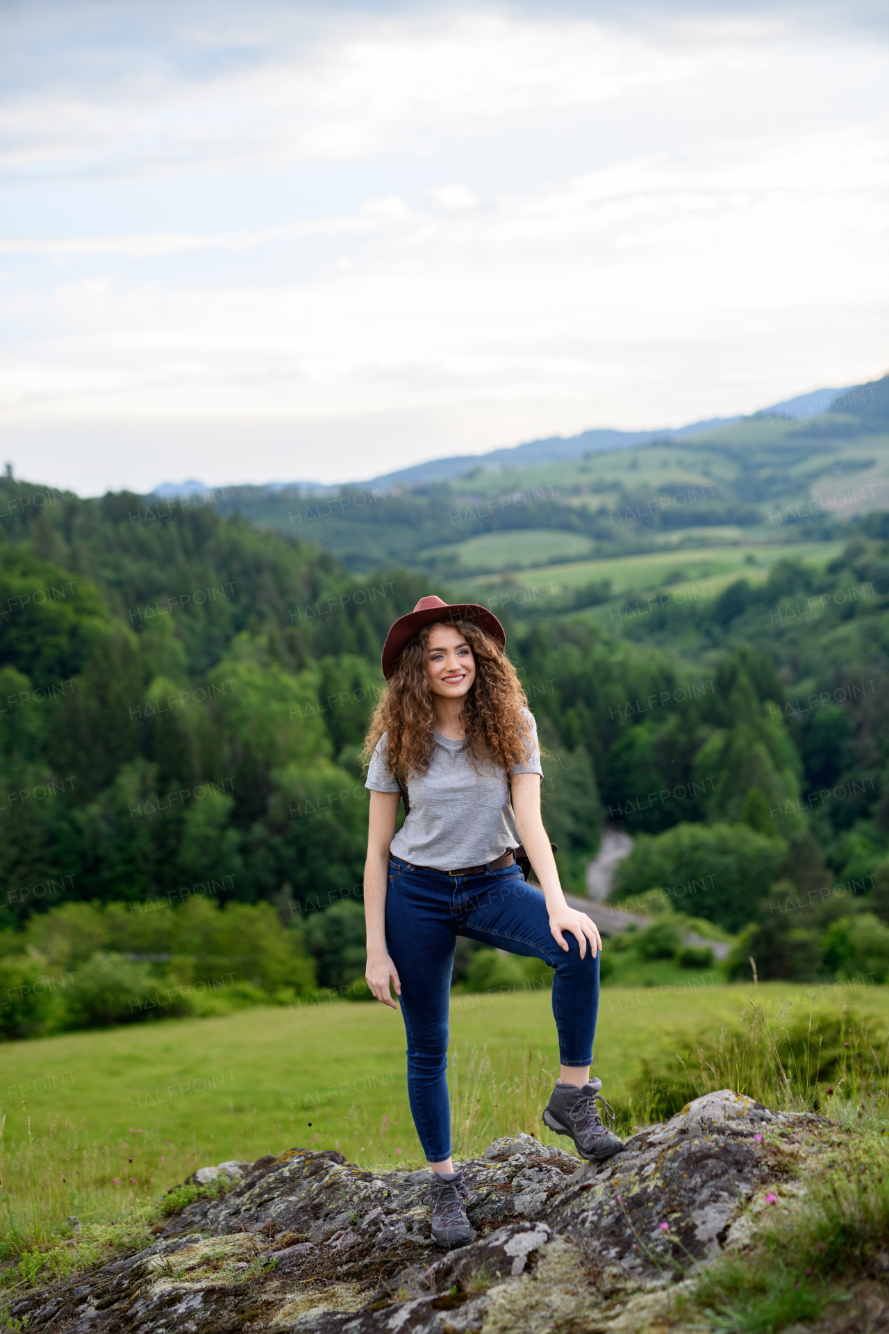 Beautiful young tourist woman traveller with backpack walking in nature. Active hiker on trail in mountains enjoying sunset. Solo summer vacation.