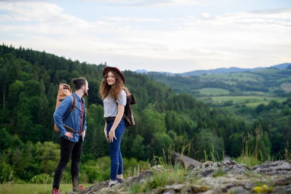 Travellers couple hiking on easy trail in nature with backpacks. Young tourist spending romantic summer vacation oudoors.