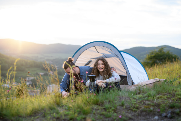 Travellers couple spending time outdoor, sleeping in tent shelter. Young tourist sitting in nature, resting, enjoying sunset. Romantic summer vacation in nature.