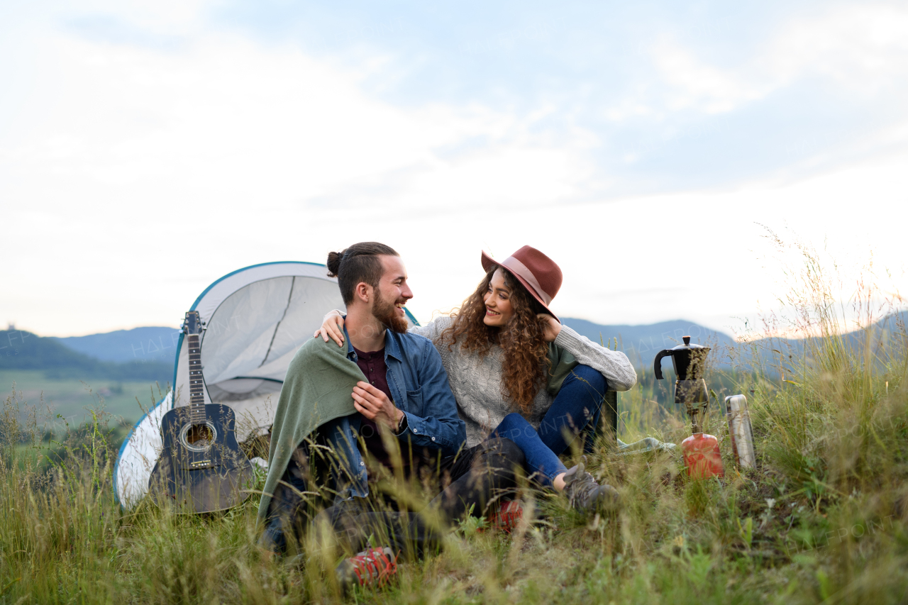 Travellers couple spending time outdoor, sleeping in tent shelter. Young tourist sitting in nature, resting, enjoying sunset. Romantic summer vacation in nature.