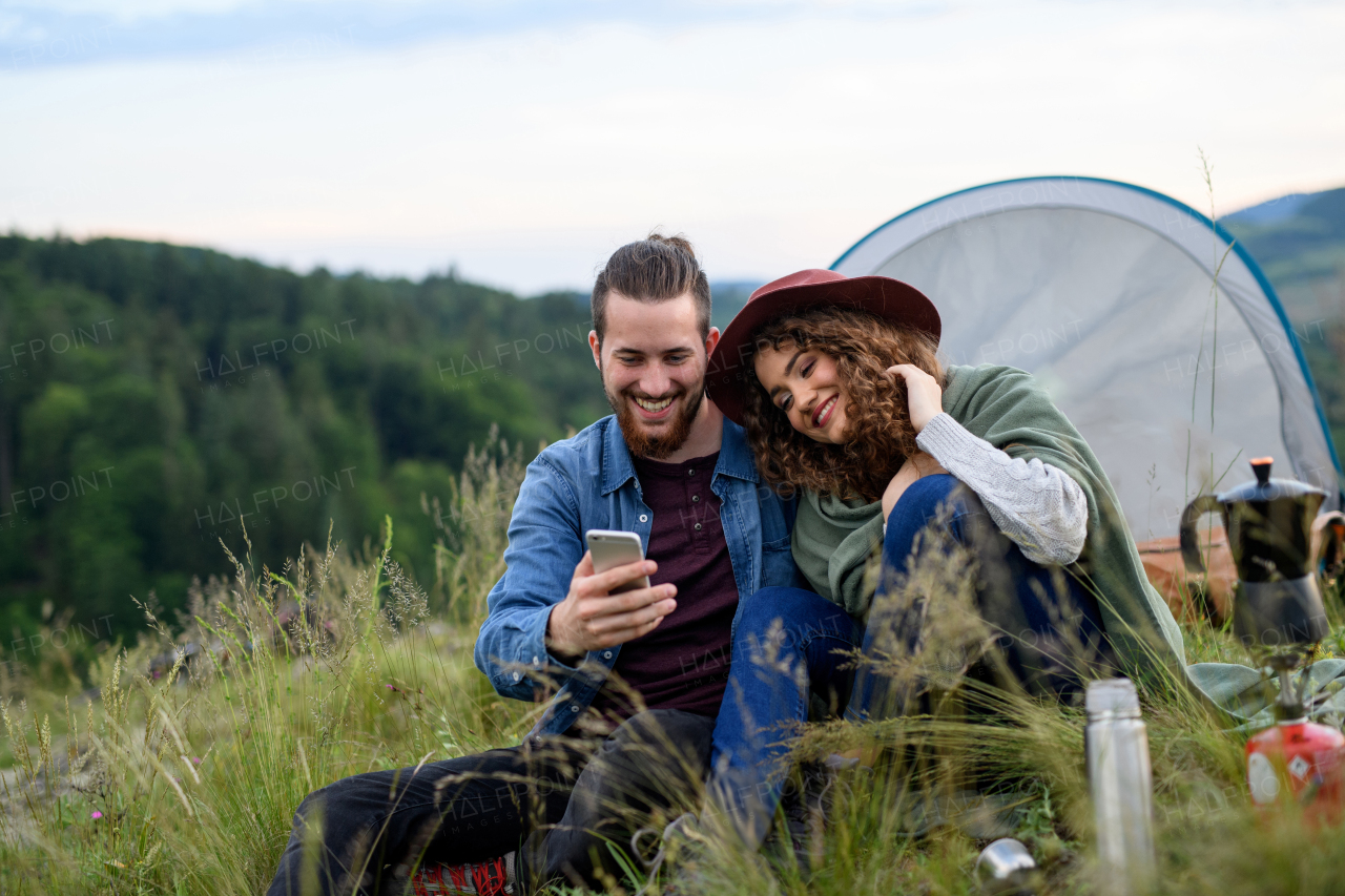 Travellers couple spending time outdoor, sleeping in tent shelter. Young tourist sitting in nature, resting, enjoying sunset. Romantic summer vacation in nature.