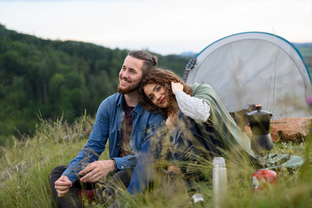 Travellers couple spending time outdoor, sleeping in tent shelter. Young tourist sitting in nature, resting, enjoying sunset. Romantic summer vacation in nature.