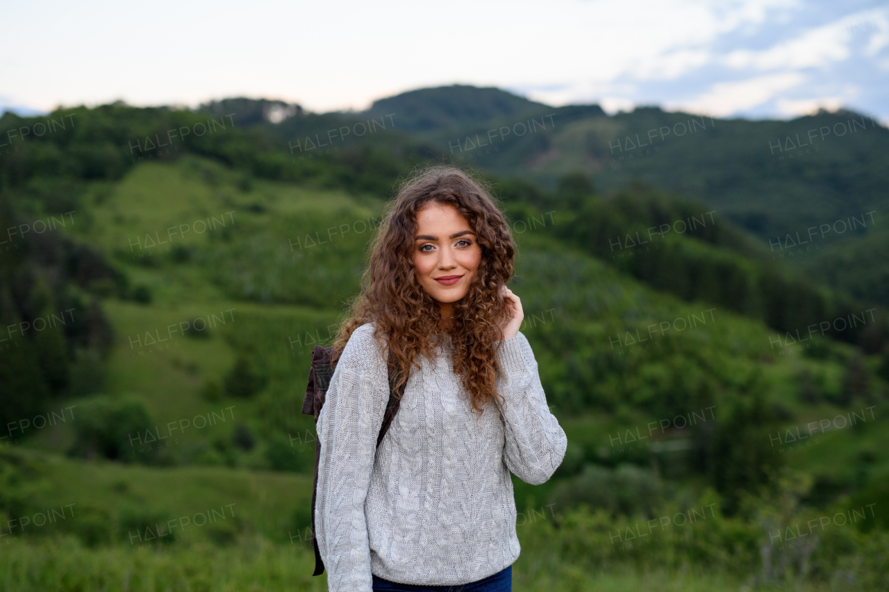 Beautiful young tourist woman traveller with backpack walking in nature. Active hiker on trail in mountains enjoying sunset. Solo summer vacation.