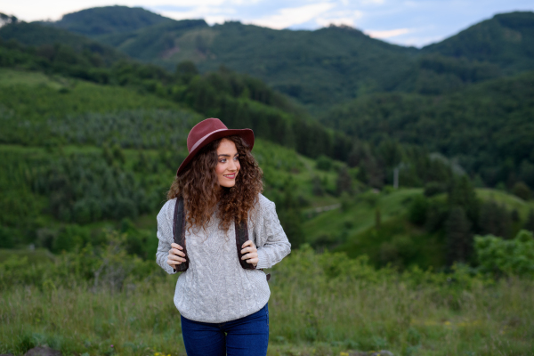 Beautiful young tourist woman traveller with backpack walking in nature. Active hiker on trail in mountains enjoying sunset. Solo summer vacation.