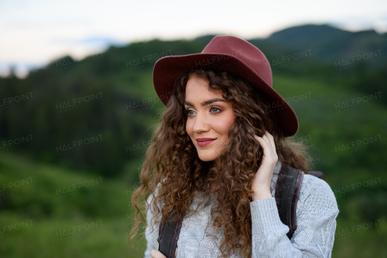 Beautiful young tourist woman traveller with backpack walking in nature. Active hiker on trail in mountains enjoying sunset. Solo summer vacation.