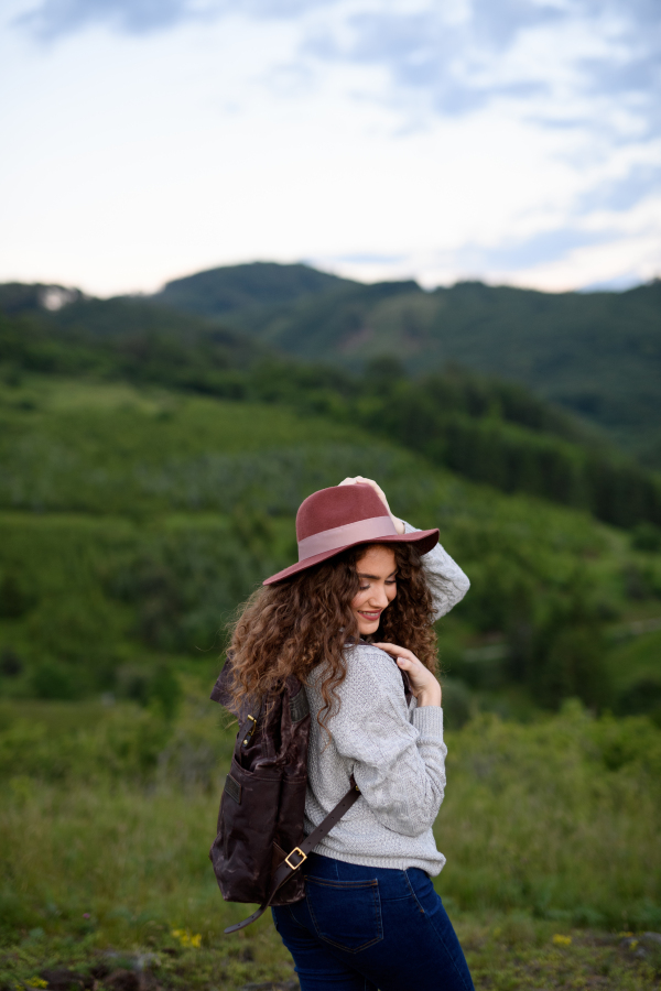 Beautiful young tourist woman traveller with backpack walking in nature. Active hiker on trail in mountains enjoying sunset. Solo summer vacation.