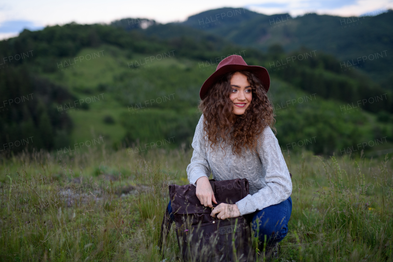 Beautiful young tourist woman traveller with backpack walking in nature. Active hiker on trail in mountains enjoying sunset. Solo summer vacation.