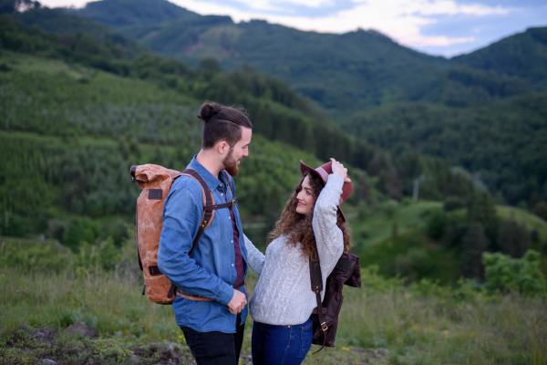 Travellers couple hiking on easy trail in nature with backpacks. Young tourist spending romantic summer vacation oudoors.