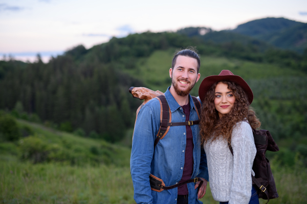 Travellers couple hiking on easy trail in nature with backpacks. Young tourist spending romantic summer vacation oudoors.