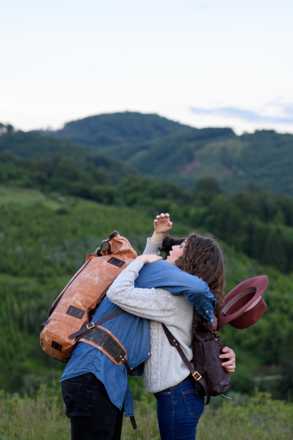 Travellers friends surprise meeting during hike in nature, embracing. Young tourist spending summer vacation oudoors.