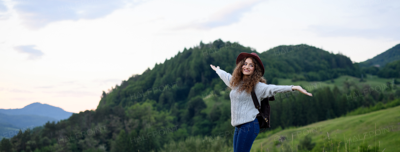 Beautiful young tourist woman traveller with backpack walking in nature. Active hiker on trail in mountains enjoying sunset. Solo summer vacation. Banner with copyspace.