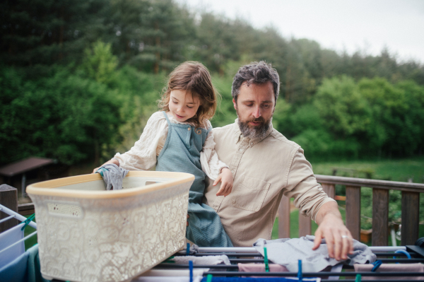 Dad embracing young daughter, carry her, looking at her lovingly, walking in spring nature. Fatherhood and Father's Day Young son helping mother with hosehold chores, hanging clothes on drying rack. Weekly chores, weekend activities for family.