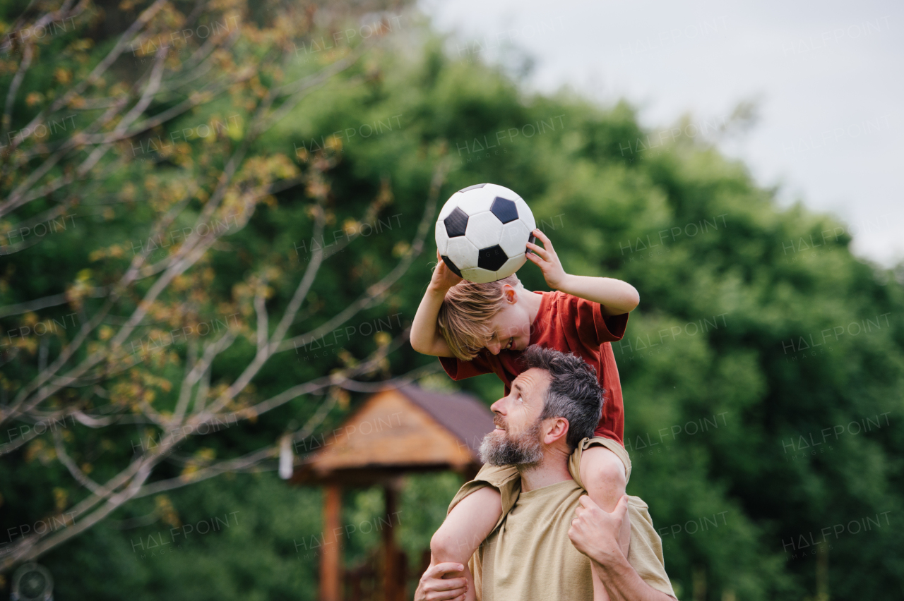 Dad having fun with young son, playing football, carrying boy on shoulders. Playing on a lawn in front of their house. Fatherhood and Father's Day concept.