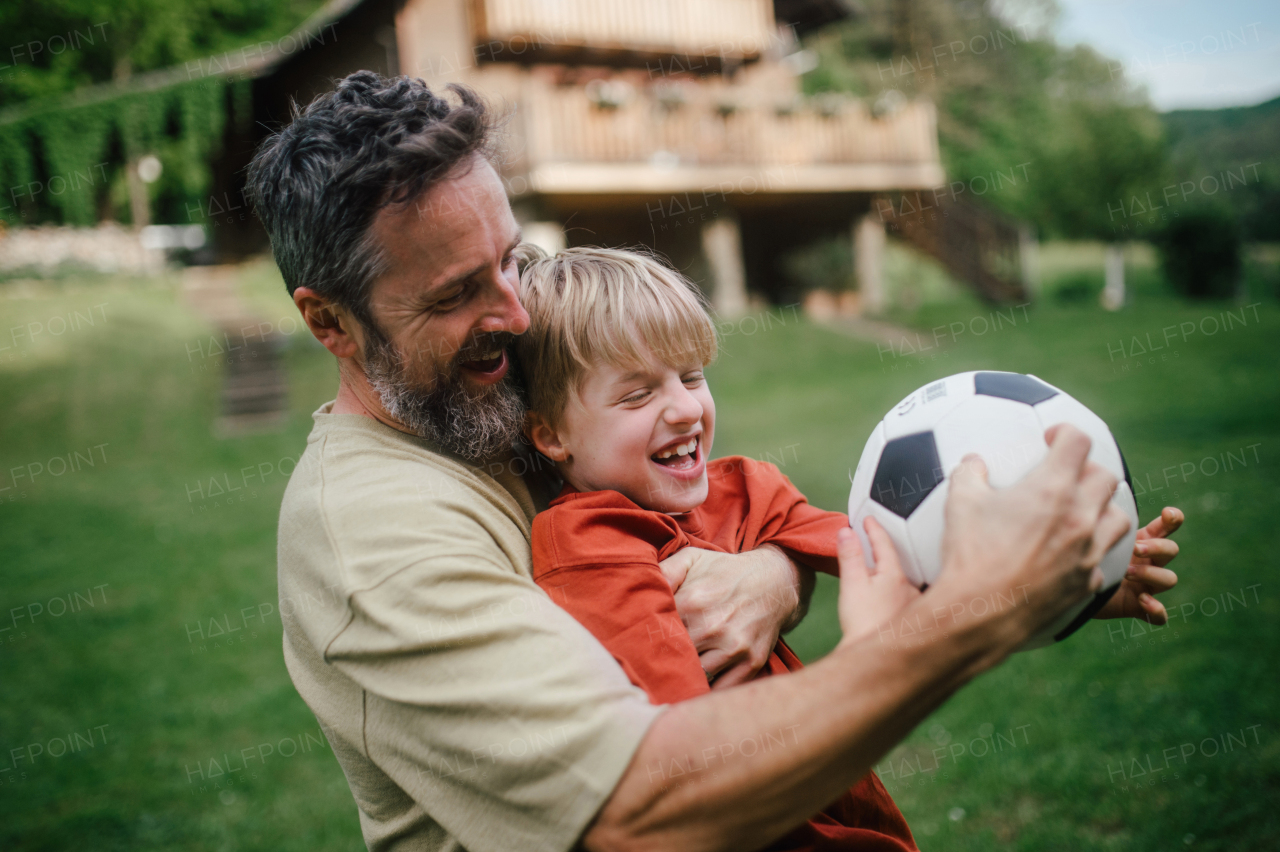 Dad having fun with young son, playing football, running and catching each other. Playing on a lawn in front of their house. Fatherhood and Father's Day concept.