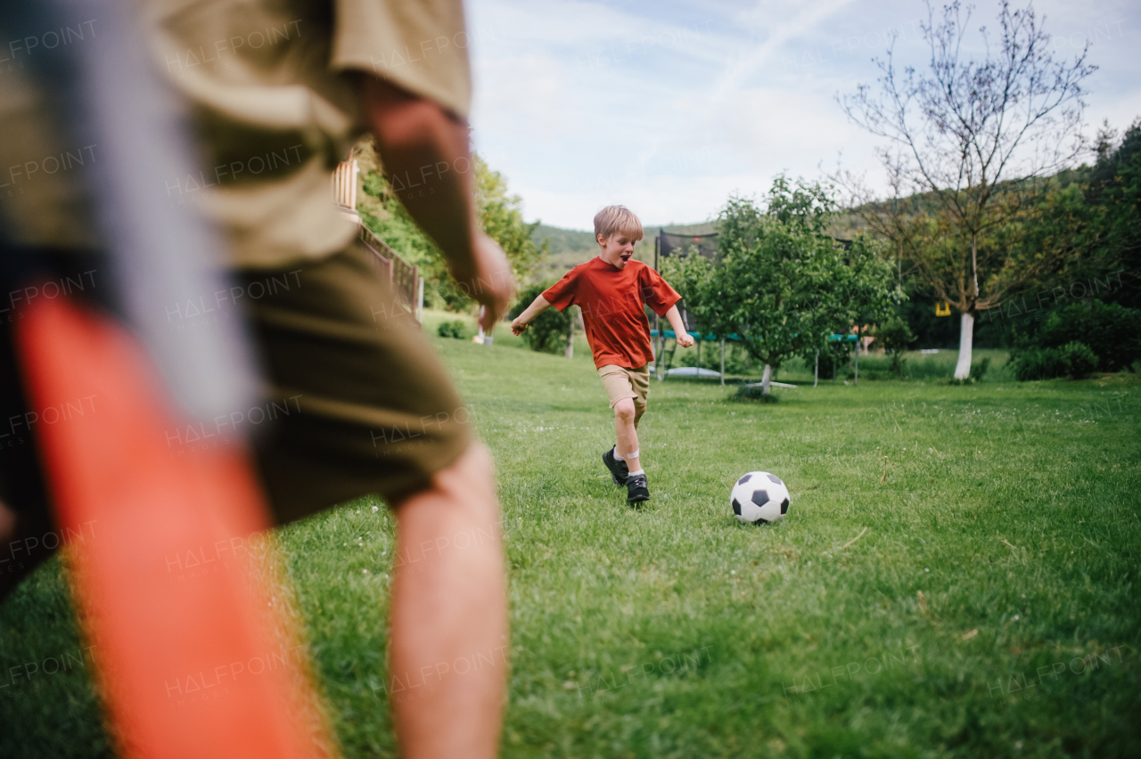 Dad having fun with young son, playing football, running and kicking ball. Playing on a lawn in front of their house. Fatherhood and Father's Day concept.