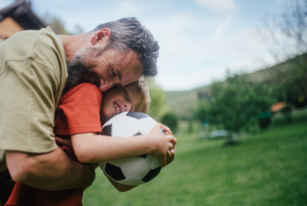 Dad having fun with young son, playing football, running and catching each other. Playing on a lawn in front of their house. Fatherhood and Father's Day concept.