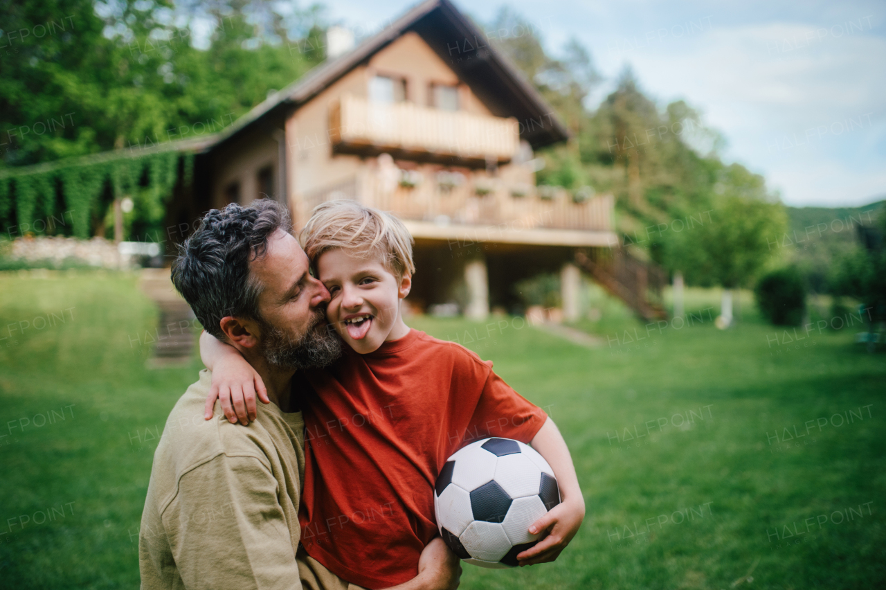 Dad having fun with young son, playing football, running and catching each other. Playing on a lawn in front of their house. Fatherhood and Father's Day concept.