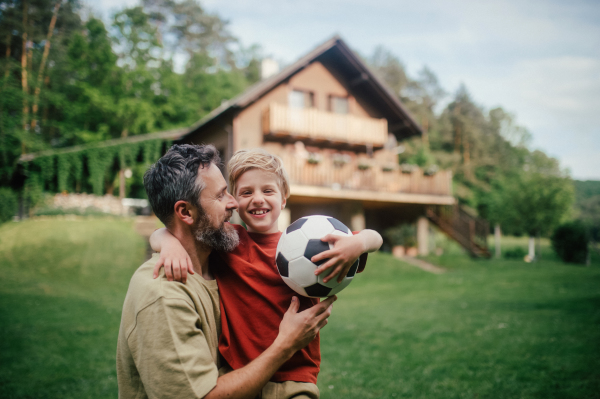 Dad embracing young son, running and celebrating the win after goal. Playing football on a lawn in front of their house. Fatherhood and Father's Day concept.