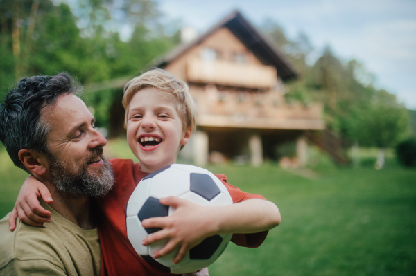 Dad having fun with young son, playing football, running and catching each other. Playing on a lawn in front of their house. Fatherhood and Father's Day concept.