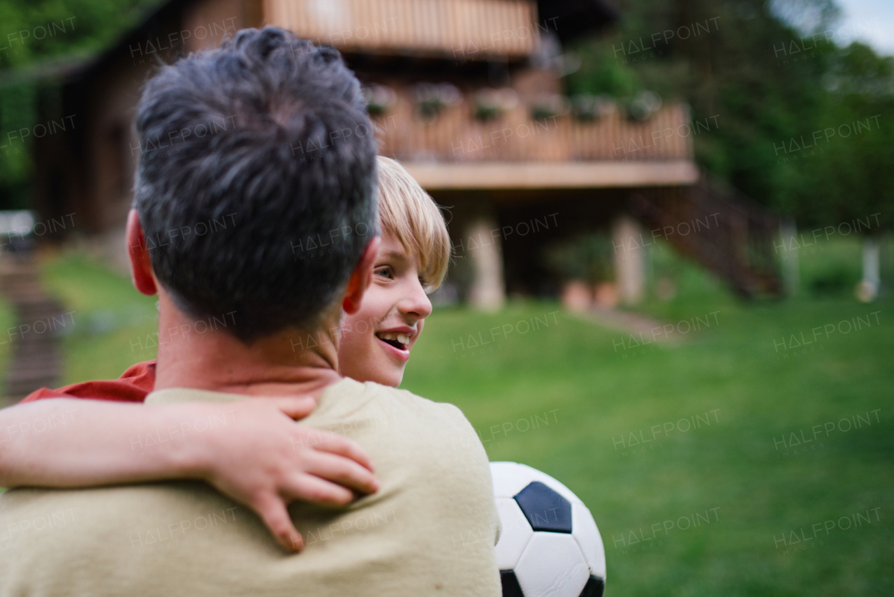 Dad embracing young son, running and celebrating the win after goal. Playing football on a lawn in front of their house. Fatherhood and Father's Day concept.