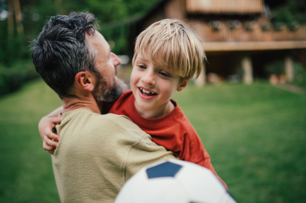 Dad having fun with young son, playing football, running and catching each other. Playing on a lawn in front of their house. Fatherhood and Father's Day concept.