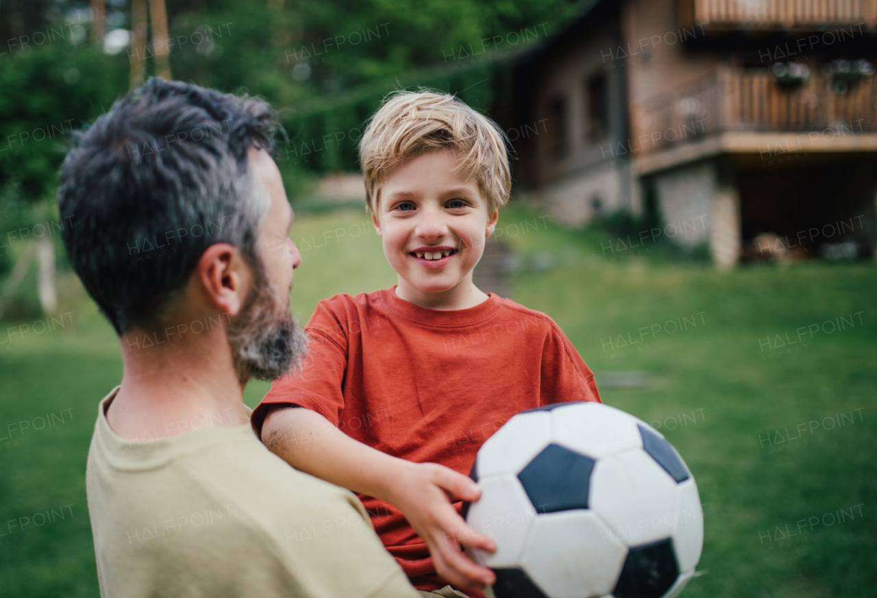 Dad having fun with young son, playing football, running and catching each other. Playing on a lawn in front of their house. Fatherhood and Father's Day concept.