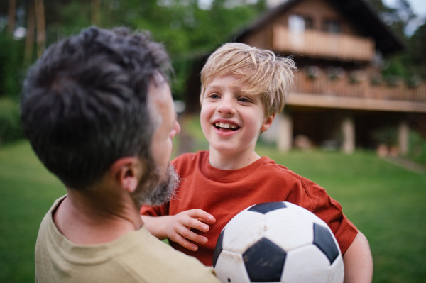 Dad embracing young son, running and celebrating the win after goal. Playing football on a lawn in front of their house. Fatherhood and Father's Day concept.