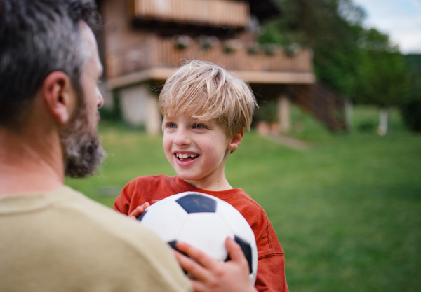 Dad embracing young son, running and celebrating the win after goal. Playing football on a lawn in front of their house. Fatherhood and Father's Day concept.