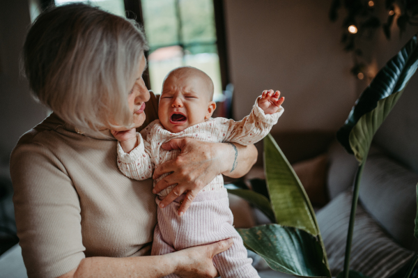 Stylish grandmother holding crying baby girl in arms, calming her down, soothing her. Strong bond between grandparent and grandchild.