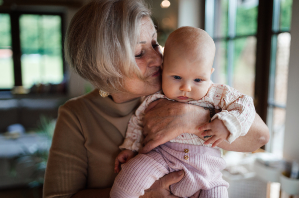 Grandmother holding little baby in arms, looking at her lovingly. Strong bond between grandparent and grandchild.