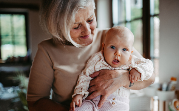 Grandmother holding little baby in arms, looking at her lovingly. Strong bond between grandparent and grandchild.