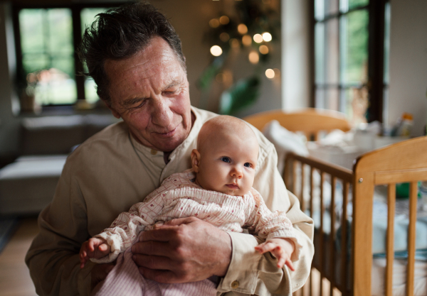 Grandfather holding little baby girl in arms, looking at her lovingly. Strong bond between grandparent and grandchild.